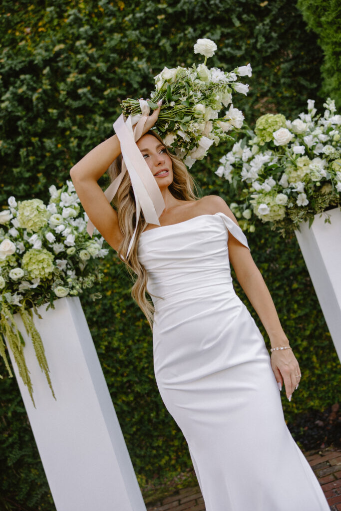 Bride holding bouquet above her head in front of lush green ceremony floral arrangements