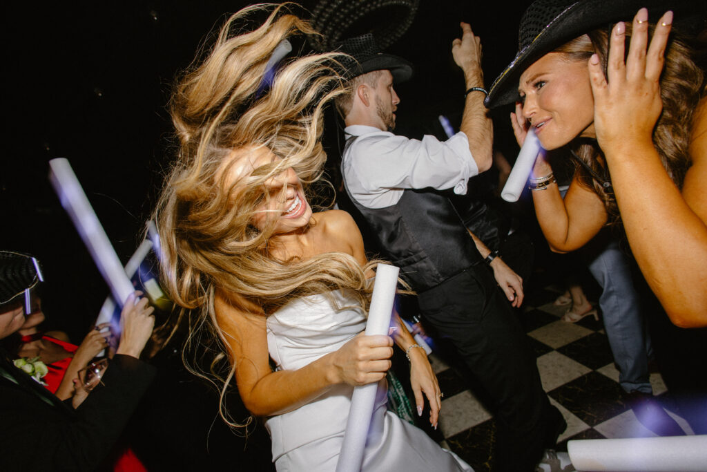 Bride dancing with friends at the wedding reception, hair flying and glow sticks in hand
