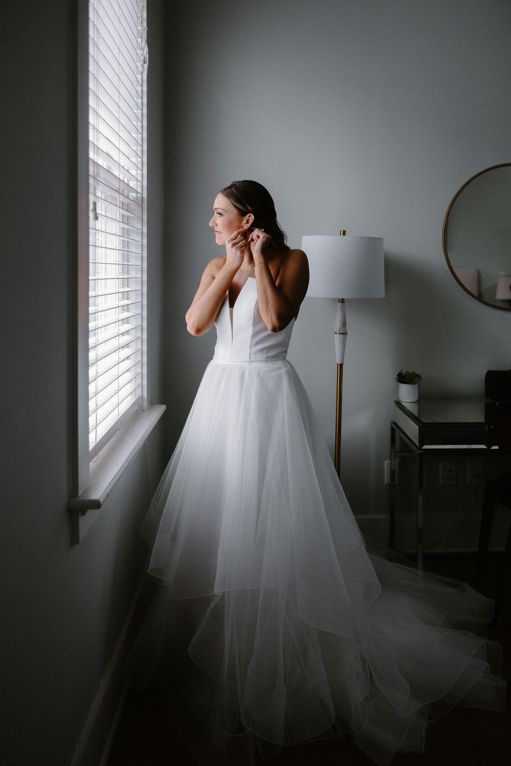 Bride Getting ready on her wedding day standing by the window putting her earrings on
