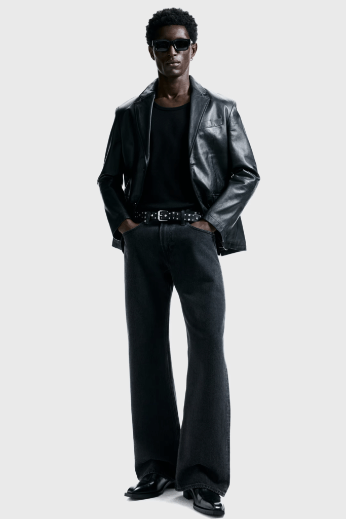 Person wearing a black leather jacket, black tank, dark flared denim, and a studded belt paired with sunglasses for an elevated edgy engagement session look.
