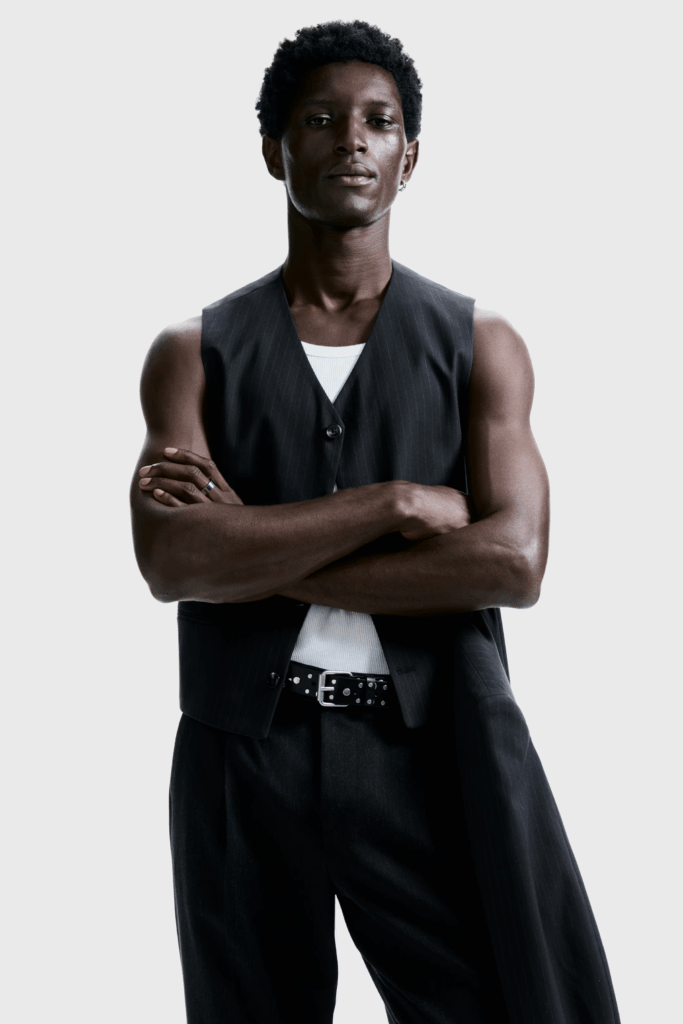 Person wearing a black pinstripe vest layered over a white tank with tailored trousers and a studded belt for a clean minimalist engagement session look.